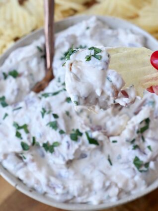 hand dipping chip into onion dip in bowl