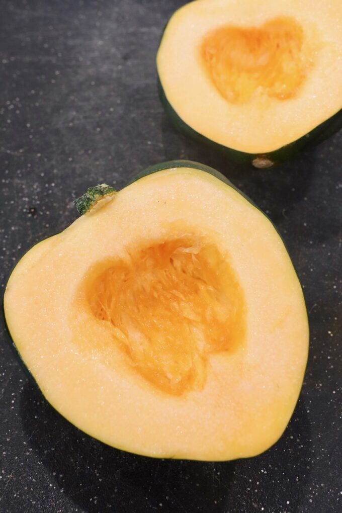 acorn squash cut in half on cutting board with the seeds removed