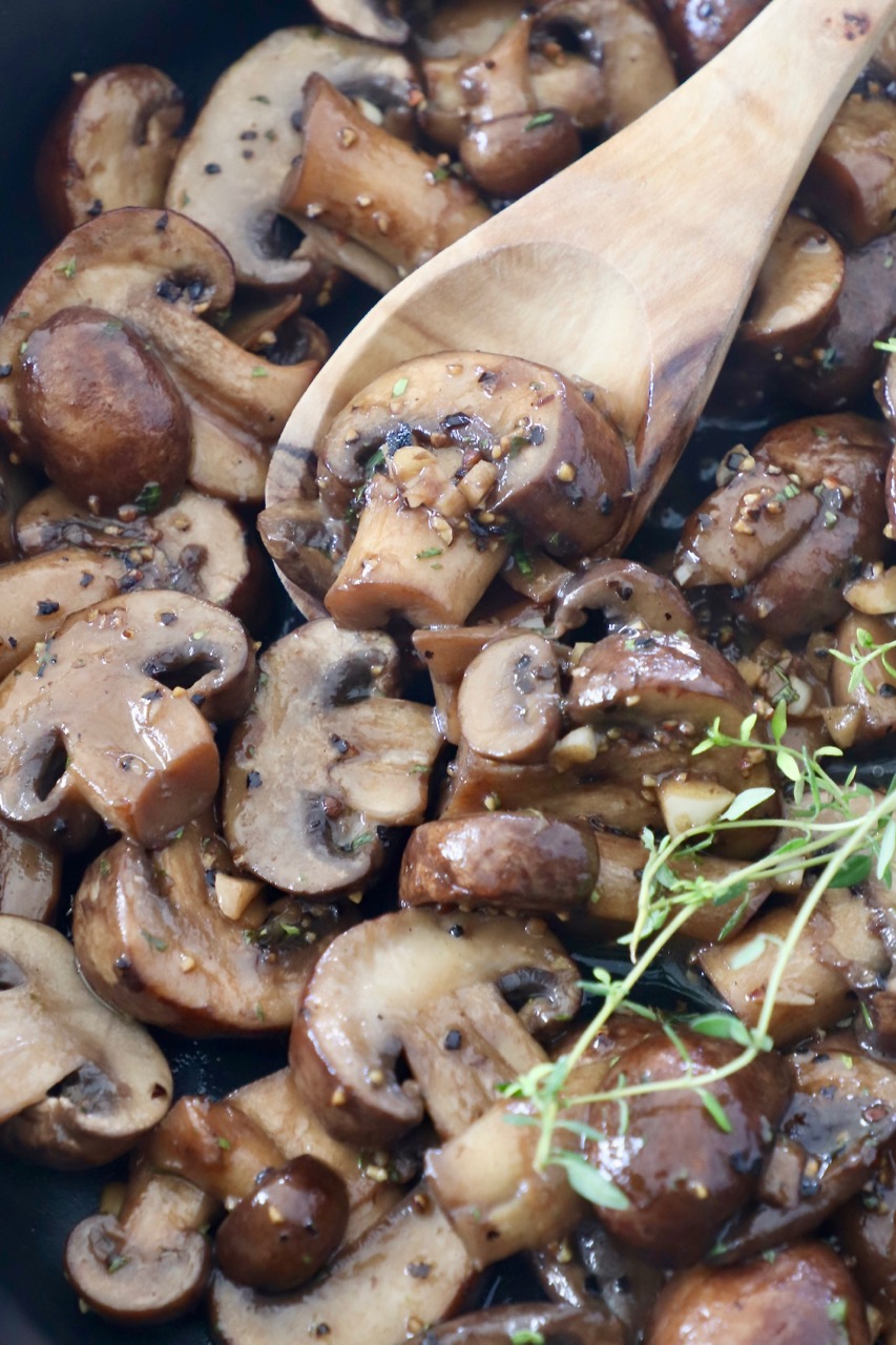 cooked sliced mushrooms in skillet with wooden spoon