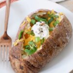 baked potato on plate with fork, filled with cheese, green onions and sour cream