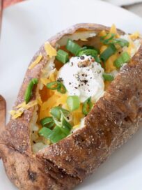 baked potato on plate with fork, filled with cheese, green onions and sour cream