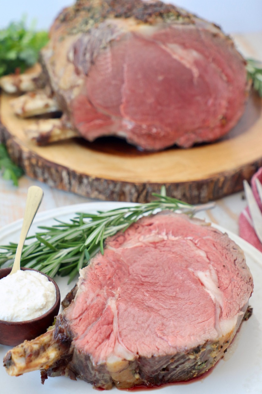 slice of prime rib on the bone on plate and whole prime rib on cutting board behind it