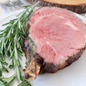 slice of bone-in prime rib on white plate with fresh rosemary sprigs