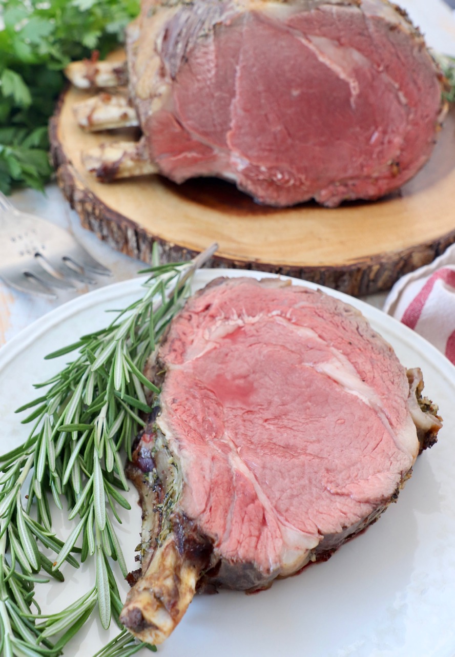 slice of prime rib with the bone on plate with fresh rosemary sprigs
