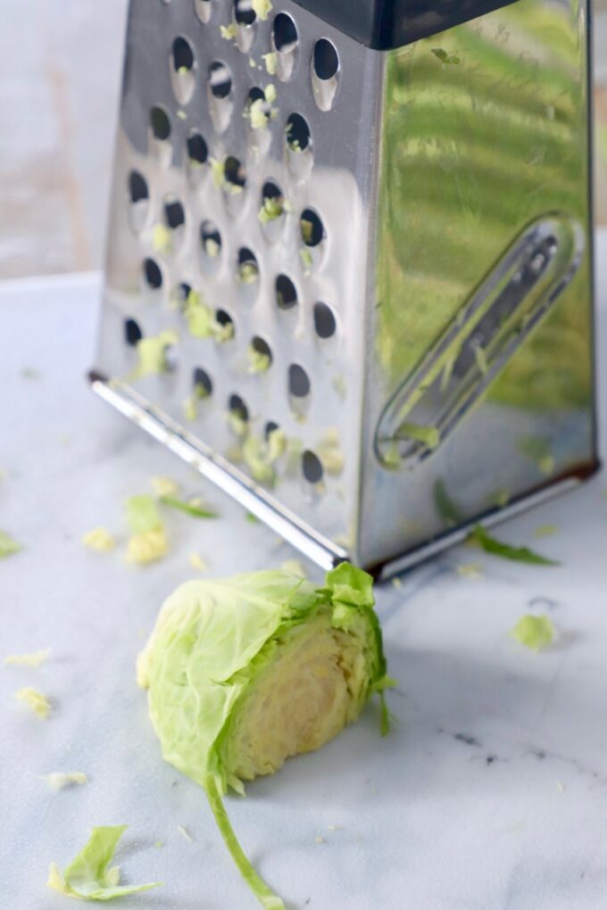 cut brussel sprout sitting in front of a box grater on a cutting board