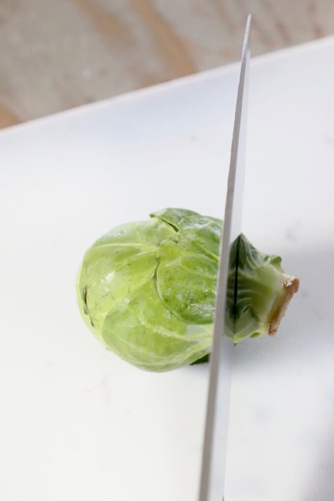 knife cutting into brussel sprout on cutting board