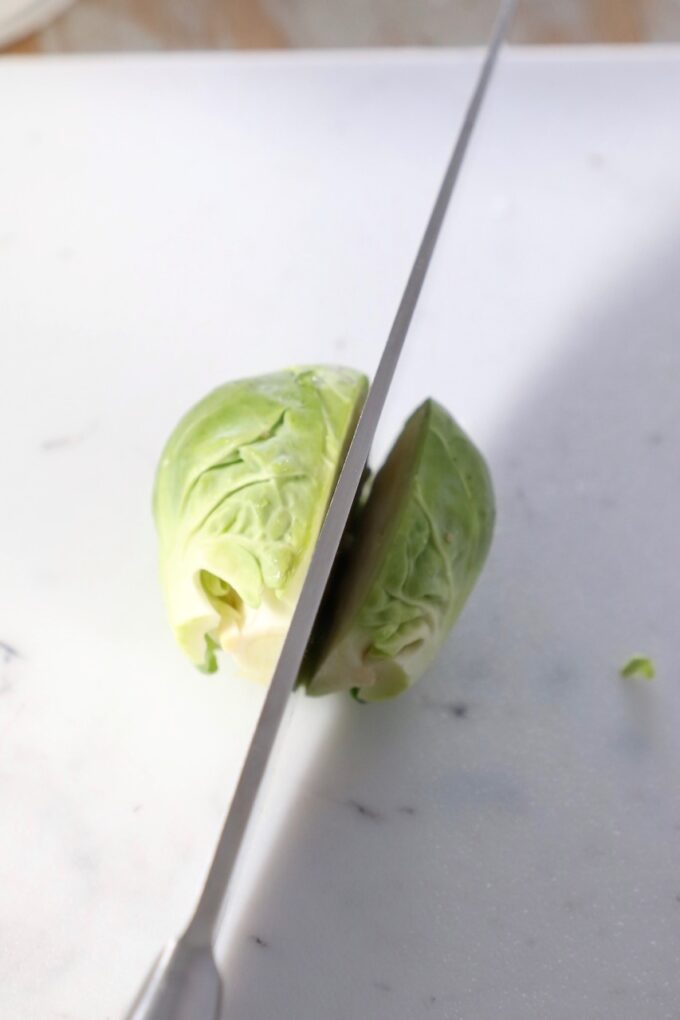 knife slicing brussel sprout in half on cutting board