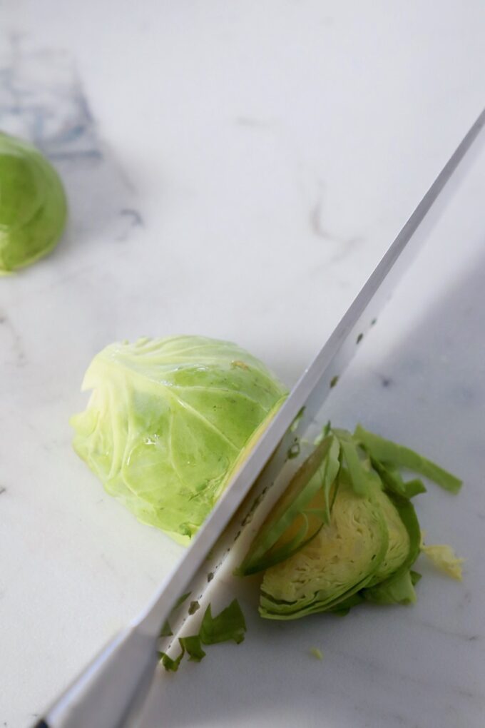 knife shredding brussel sprout on cutting board