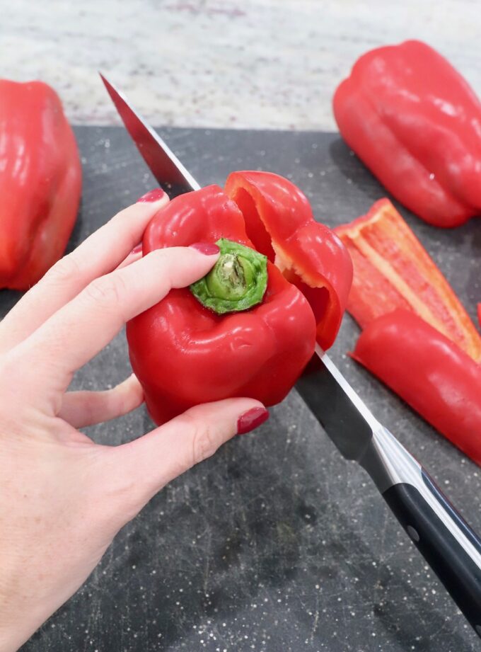 knife slicing into red bell pepper on cutting board