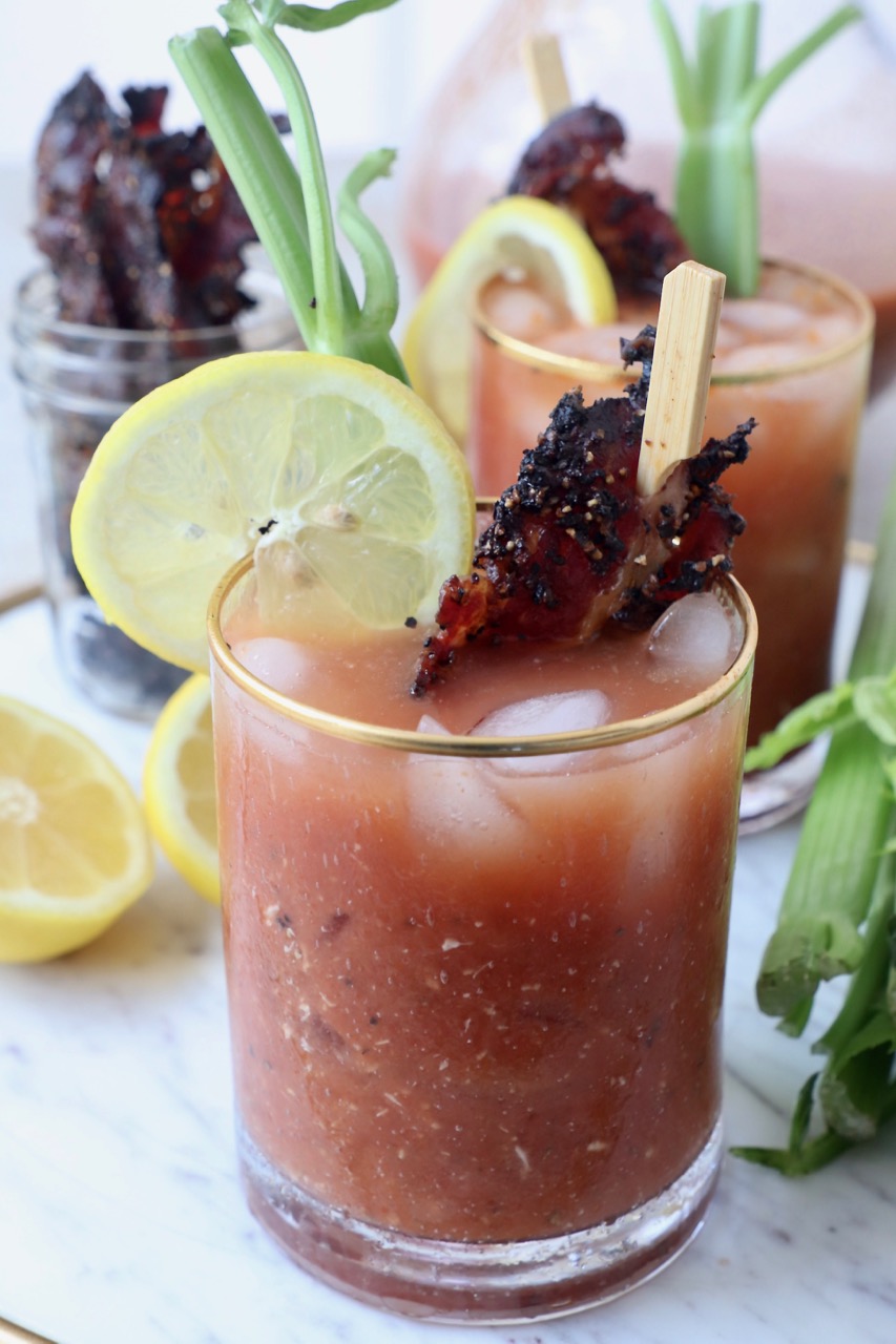 bloody mary in glass with candied bacon and lime wedge