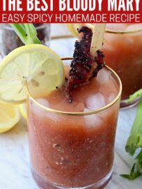 bloody mary in glass with skewer of cooked bacon, lemon slice and celery stick
