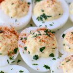 prepared deviled eggs topped with parsley and paprika on white plate