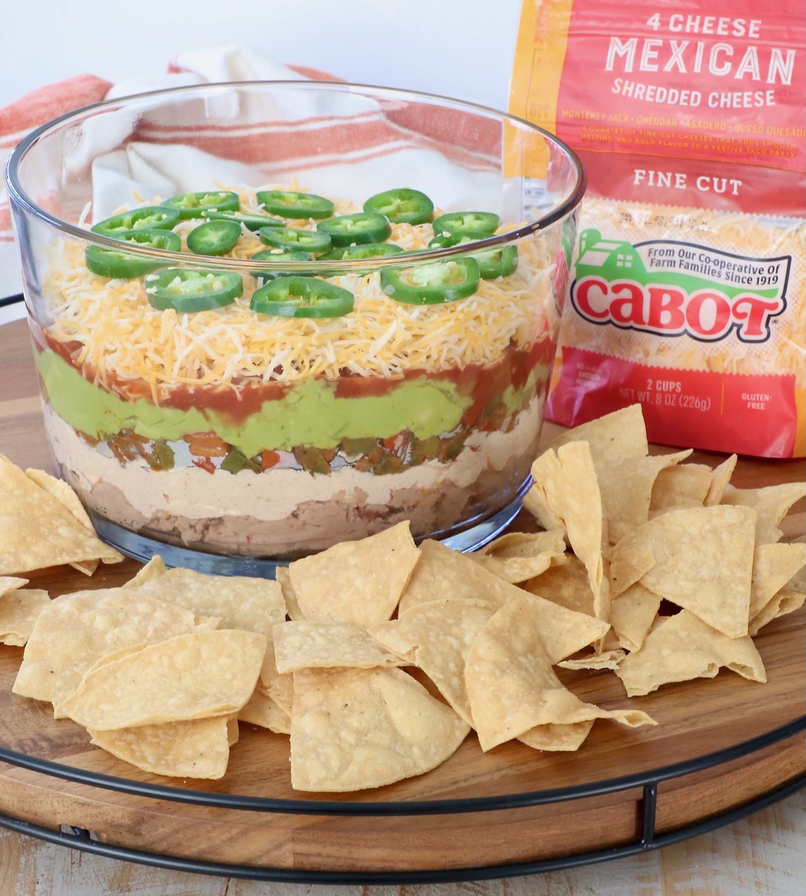 7 layer dip in glass trifle surrounded by tortilla chips on serving tray