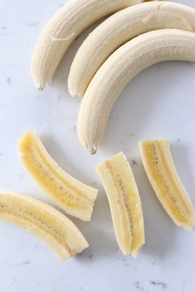 peeled bananas on cutting board, one sliced into quarters