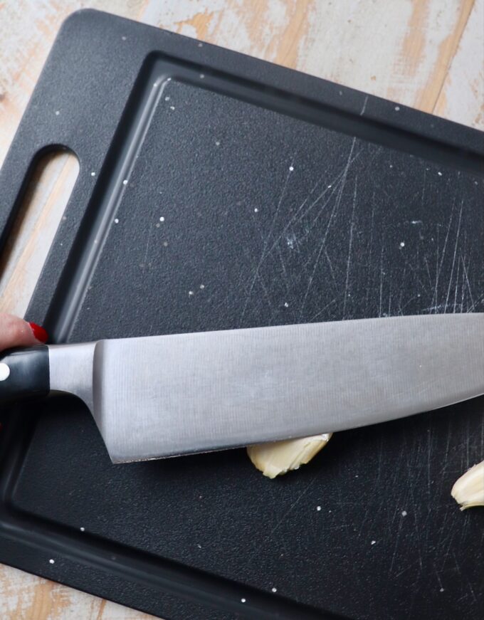 knife smashing garlic clove on cutting board