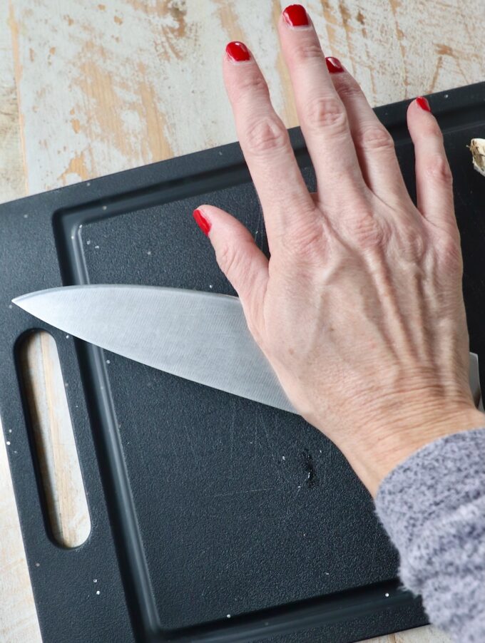 hand pressing knife on garlic clove on black cutting board