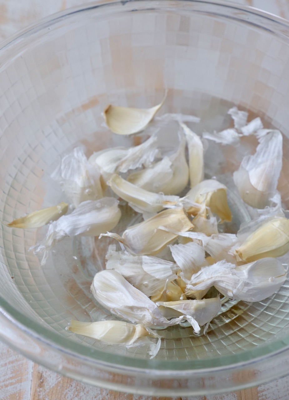unpeeled garlic cloves in glass bowl of water