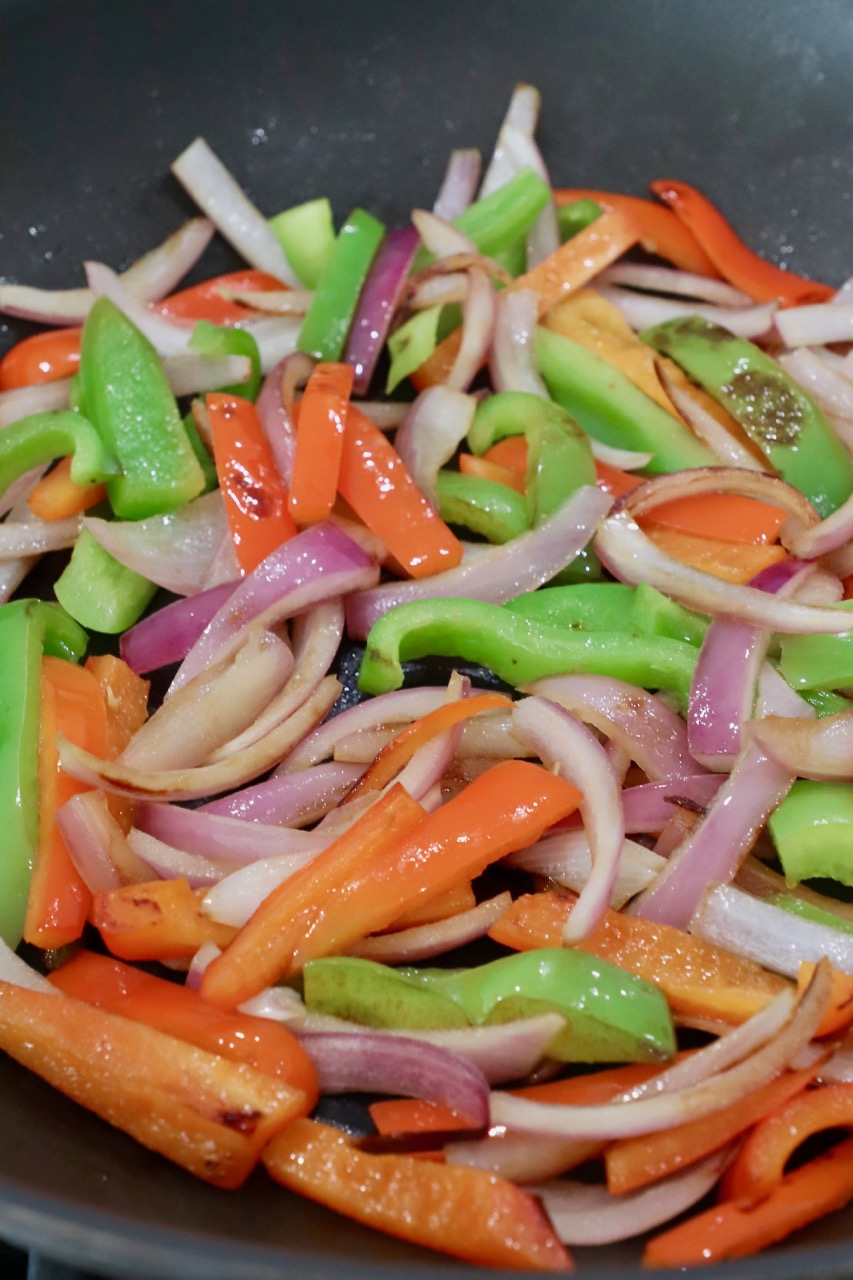 cooked sliced bell peppers and onions in skillet