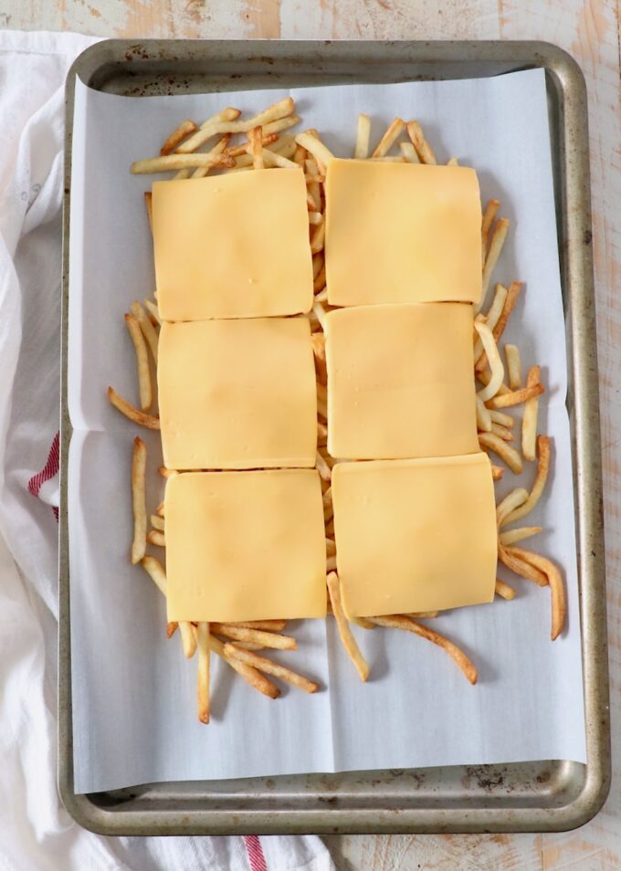cooked fresh fries on baking sheet topped with slices of cheese