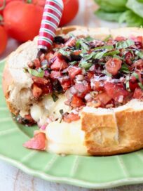 bruschetta in a bread bowl with baked brie on green plate