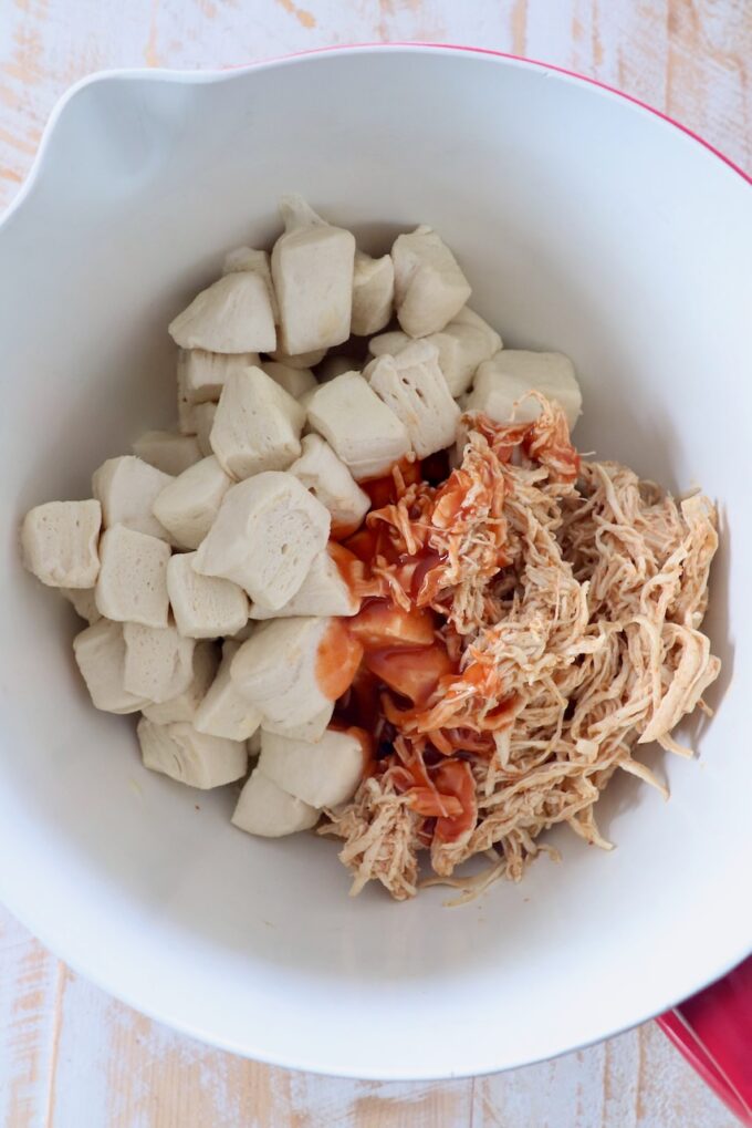 diced refrigerated biscuits, shredded chicken and buffalo sauce in mixing bowl