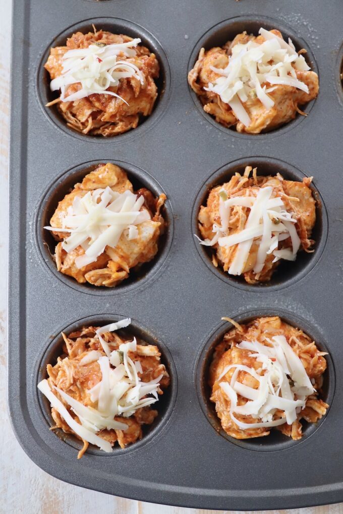 buffalo chicken rolls in muffin tin topped with shredded cheese