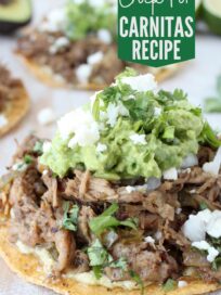 tostada topped with cooked shredded pork, guacamole and crumbled cheese