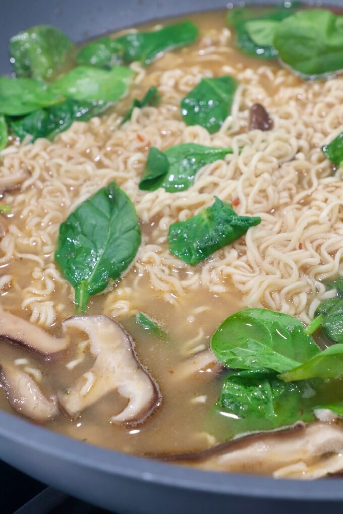 spinach, mushrooms and ramen noodles in broth in wok