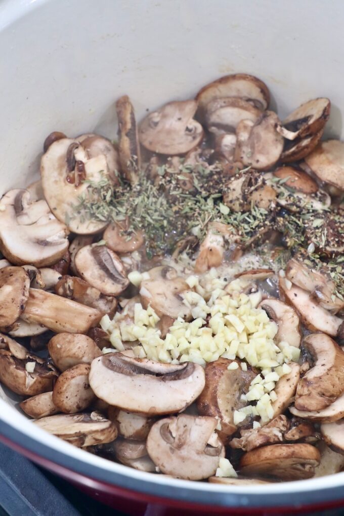 sliced mushrooms in pot with minced garlic, herbs and spices
