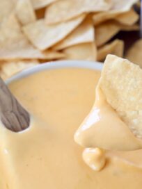 tortilla chip dipped into bowl of nacho cheese sauce