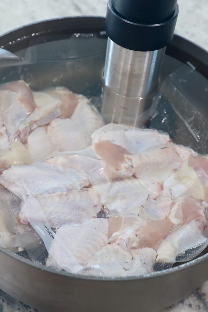 vacuum sealed bags of chicken wings in pot of water with sous vide attachment on the side