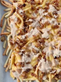 cooked french fries covered in cheese, sauce and caramelized onions on baking sheet