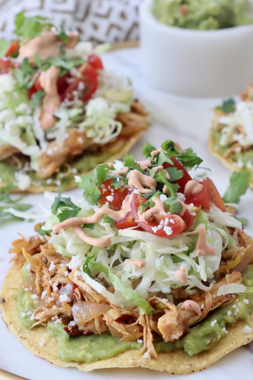 chicken tostada on plate topped with lettuce, tomato and creamy chipotle sauce
