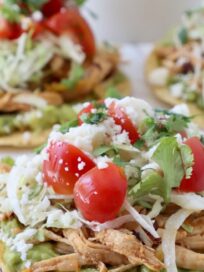 shredded chicken tostadas with guacamole, cherry tomatoes, shredded lettuce and cilantro