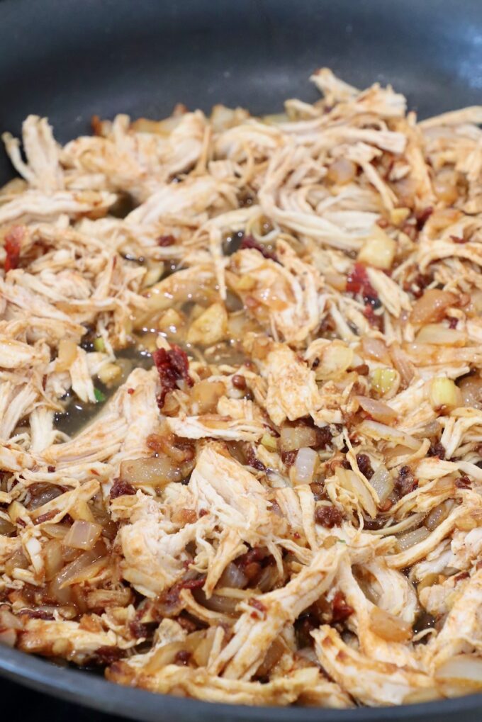 cooked, shredded chicken in skillet tossed with chili peppers and spices
