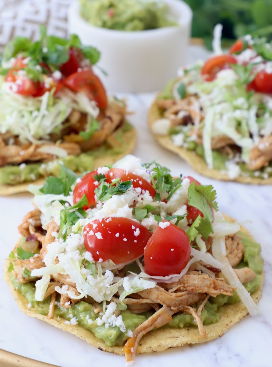 shredded chicken on tostadas with guacamole, cherry tomatoes and shredded lettuce