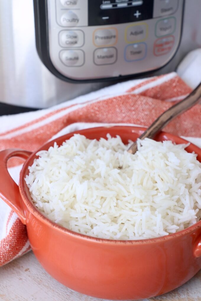 white rice in orange bowl with spoon, with Instant Pot in the background