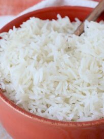 cooked white rice in orange bowl with spoon