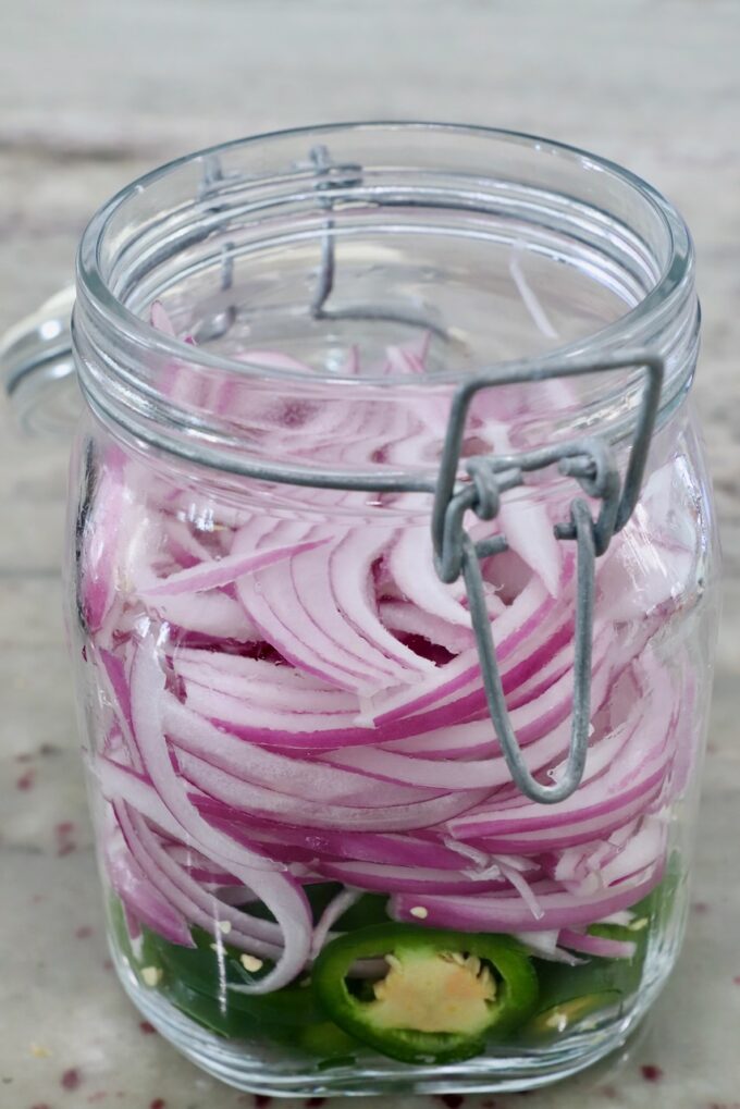 sliced red onions and jalapenos in large glass jar
