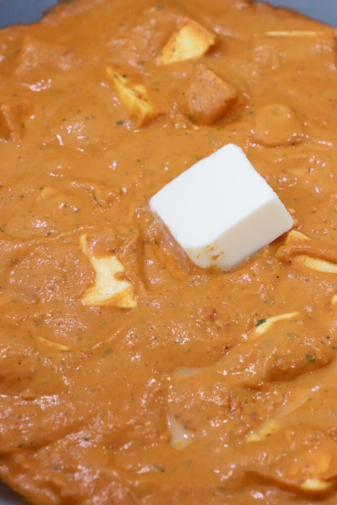 paneer in curry sauce in large pan topped with a cube of butter