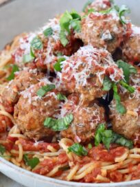 cooked meatballs tossed in tomato sauce topped with parmesan cheese and chopped basil in bowl