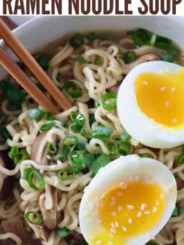 ramen noodle soup in bowl with chopsticks, topped with diced green onions and a soft boiled egg, cut in half