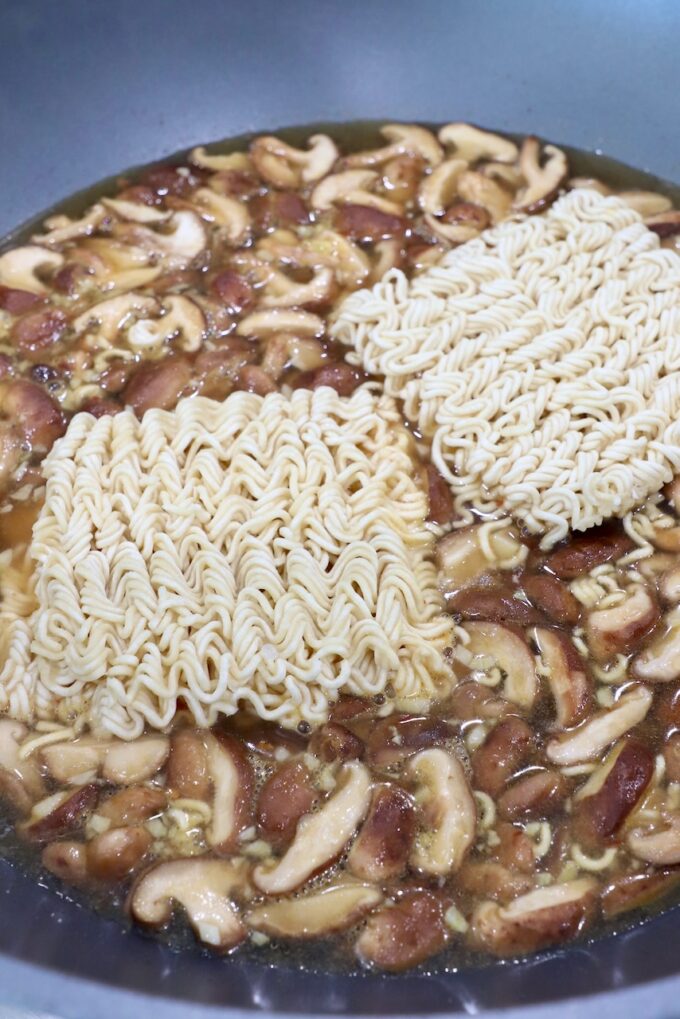 ramen noodles in large pot on stove with sliced mushrooms and broth