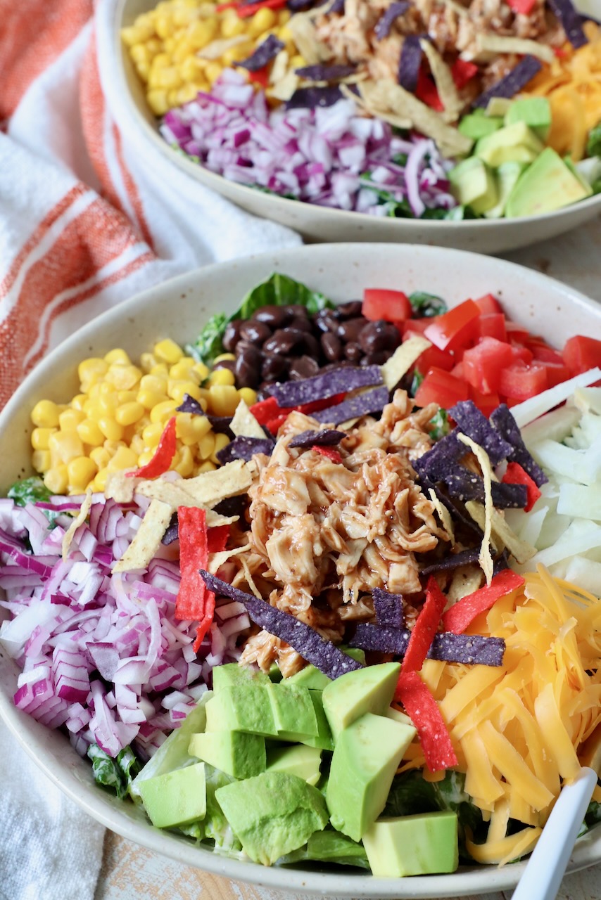 bbq chicken salad in bowl with diced onion, avocado, tomatoes, corn, black beans and cheddar cheese