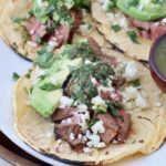 grilled diced steak in tacos with avocado and chimichurri sauce on white plate