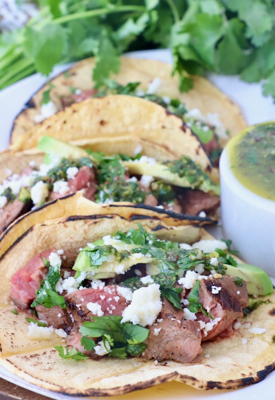 grilled steak in tacos on plate topped with cilantro and avocado