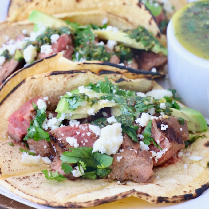 grilled steak in tacos on plate topped with cilantro and avocado