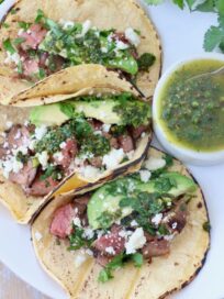 steak tacos topped with cilantro and avocado on plate with chimichurri sauce