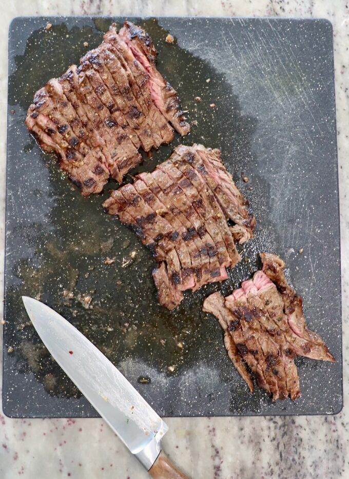 sliced grilled skirt steak on cutting board with large knife