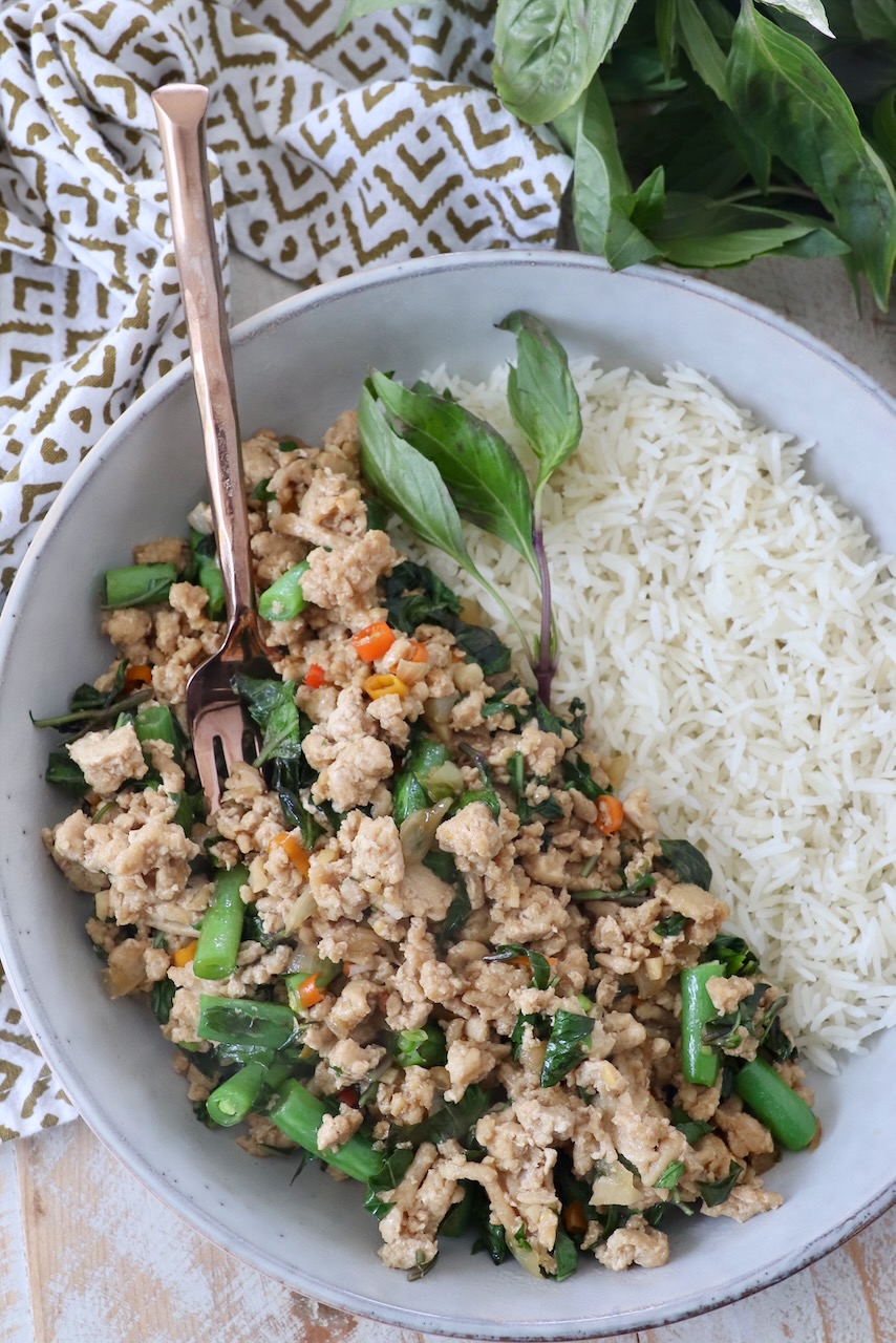 prepared thai basil chicken in bowl with cooked white rice and fresh thai basil leaves